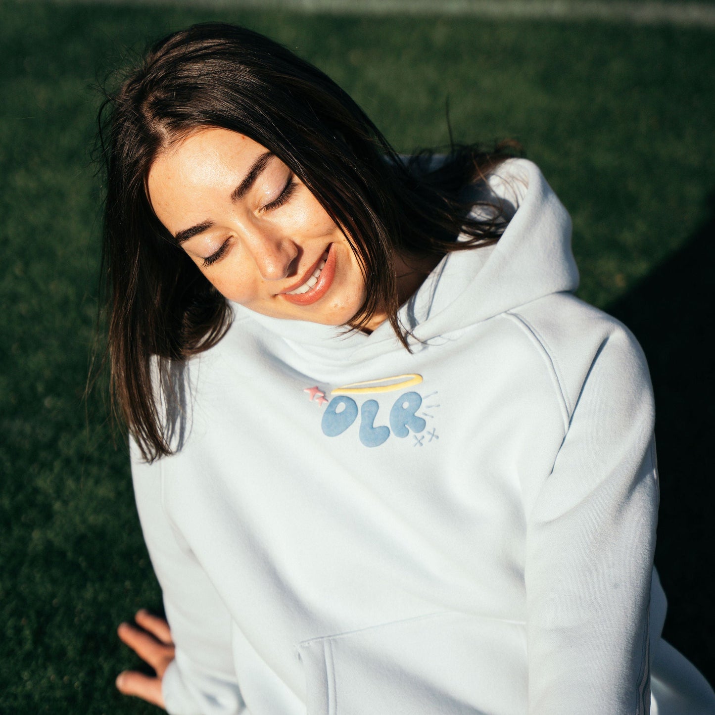 girl wearing a baby blue hoodie with a logo on a grassy background