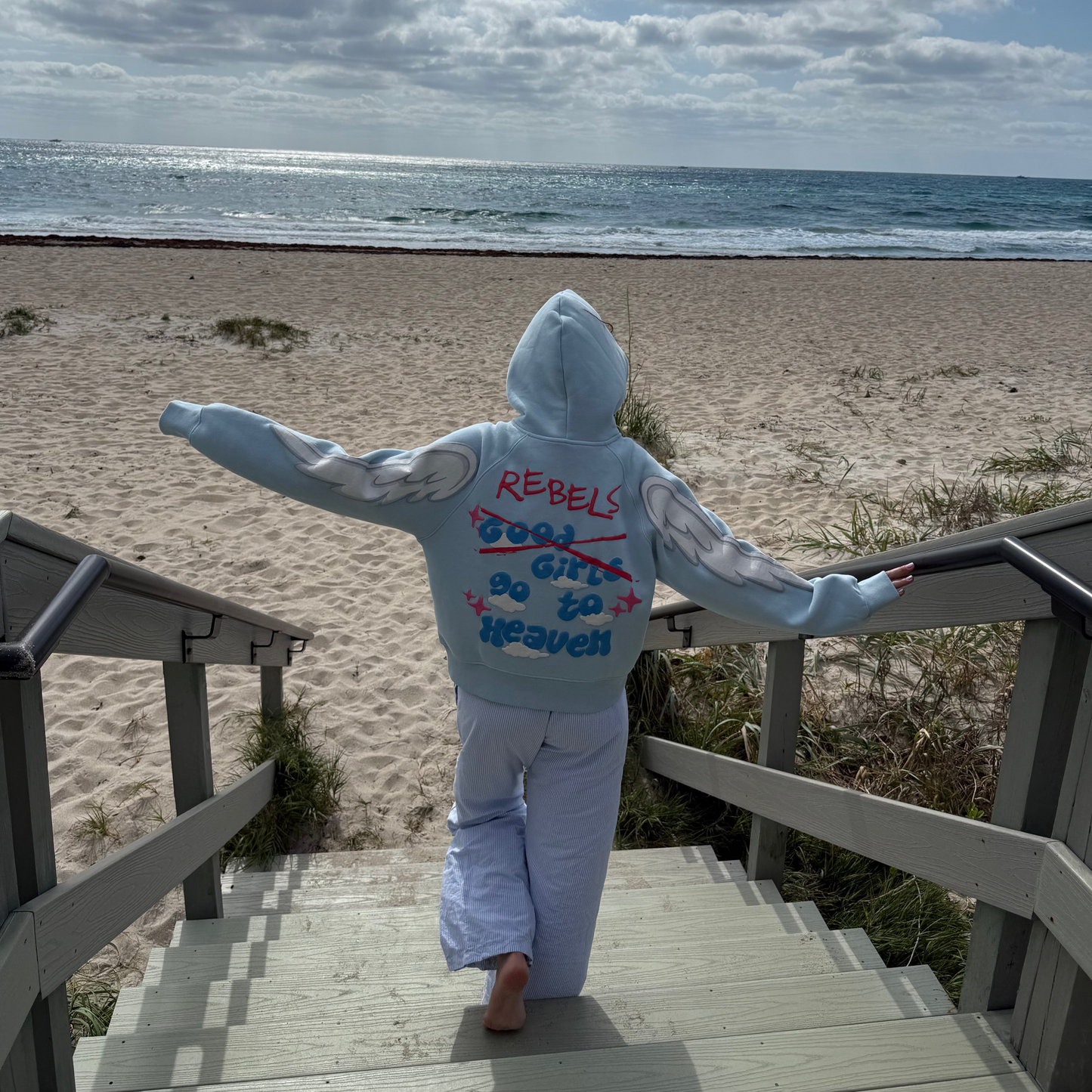 Person in a hoodie standing on a beach with ocean and sky in the background