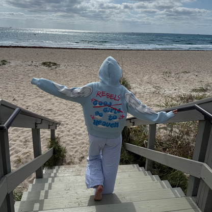 Person in a hoodie standing on a beach with ocean and sky in the background